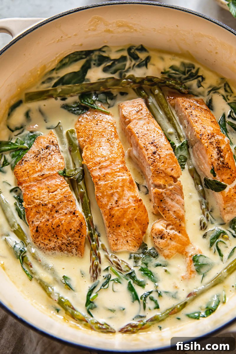 salmon in a pan with creamy sauce and greens