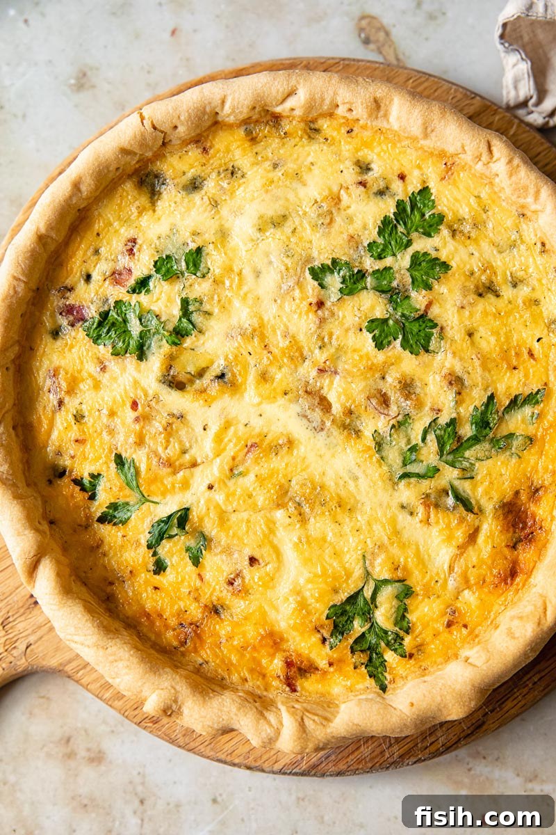 Gourmet Bacon Stilton Caramelised Onion Quiche 2 Top down view of a freshly baked Bacon, Blue Cheese, and Caramelized Onion Quiche on a round wooden cutting board, ready to be served.