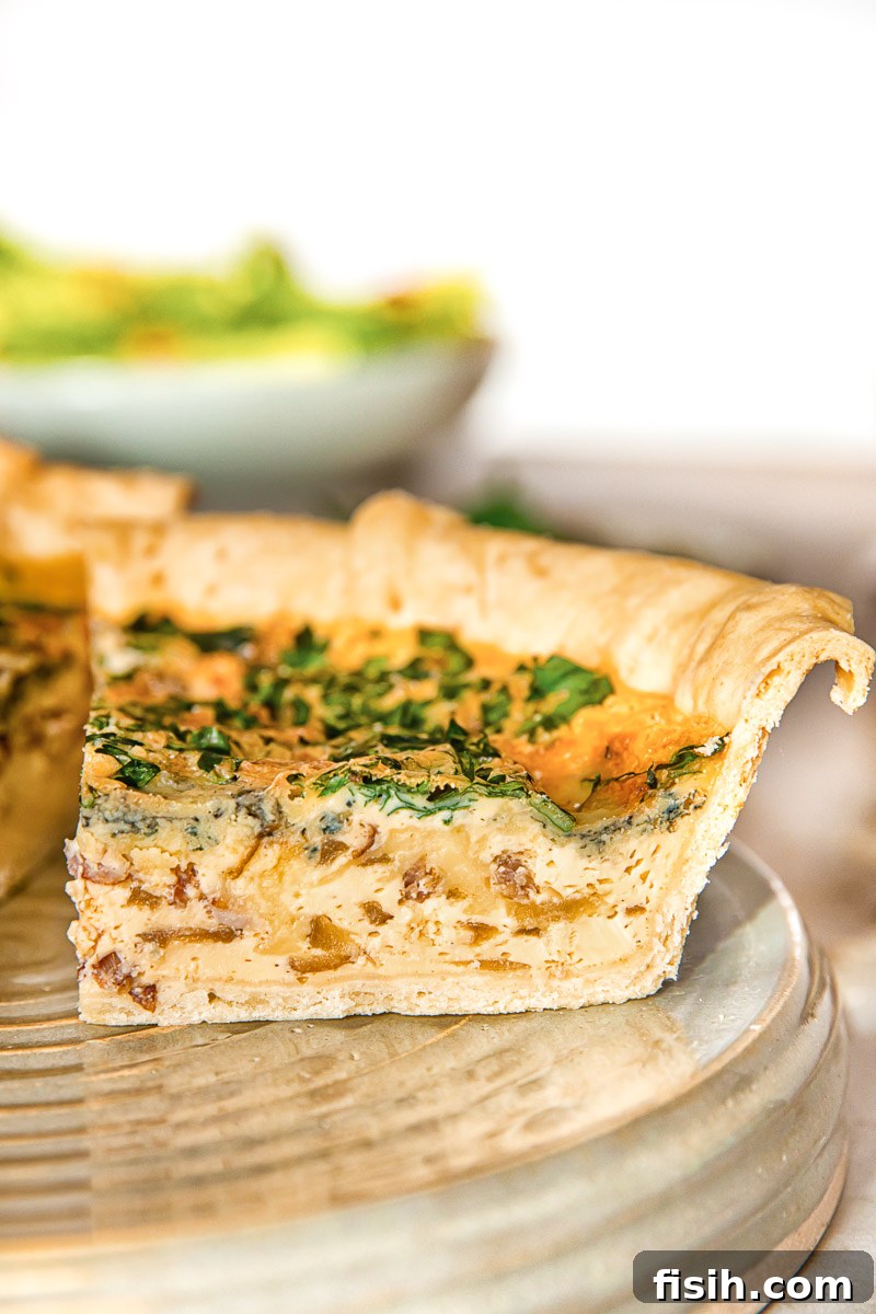 Gourmet Bacon Stilton Caramelised Onion Quiche 6 A close-up shot of a single slice of quiche, showcasing the crispy crust and the rich, creamy filling with visible pieces of bacon, blue cheese, and caramelized onion.