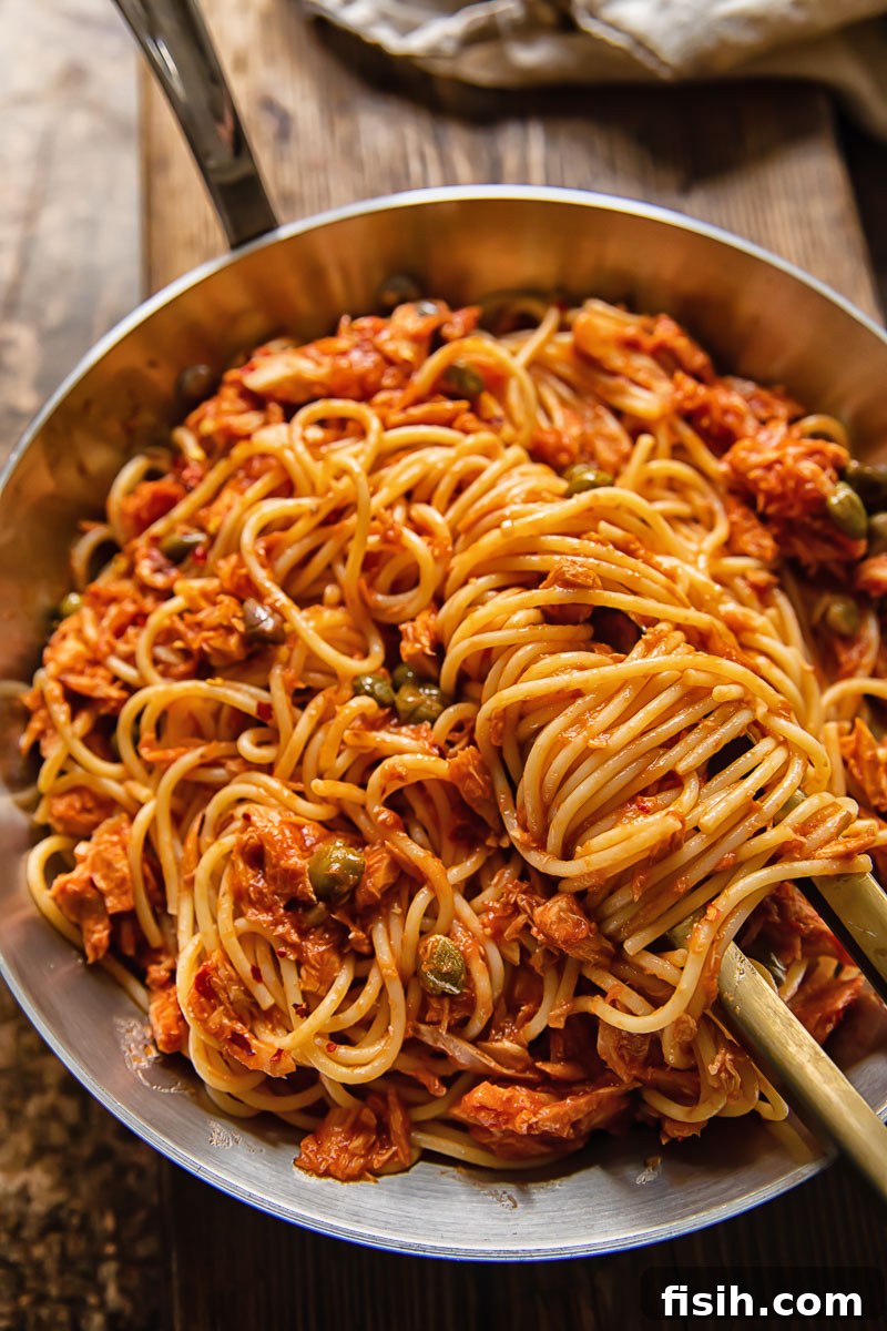 Tangy Tuna Pasta in Minutes 2 Top-down view of spaghetti in a rich red tuna and tomato sauce in a pan, garnished with fresh parsley.