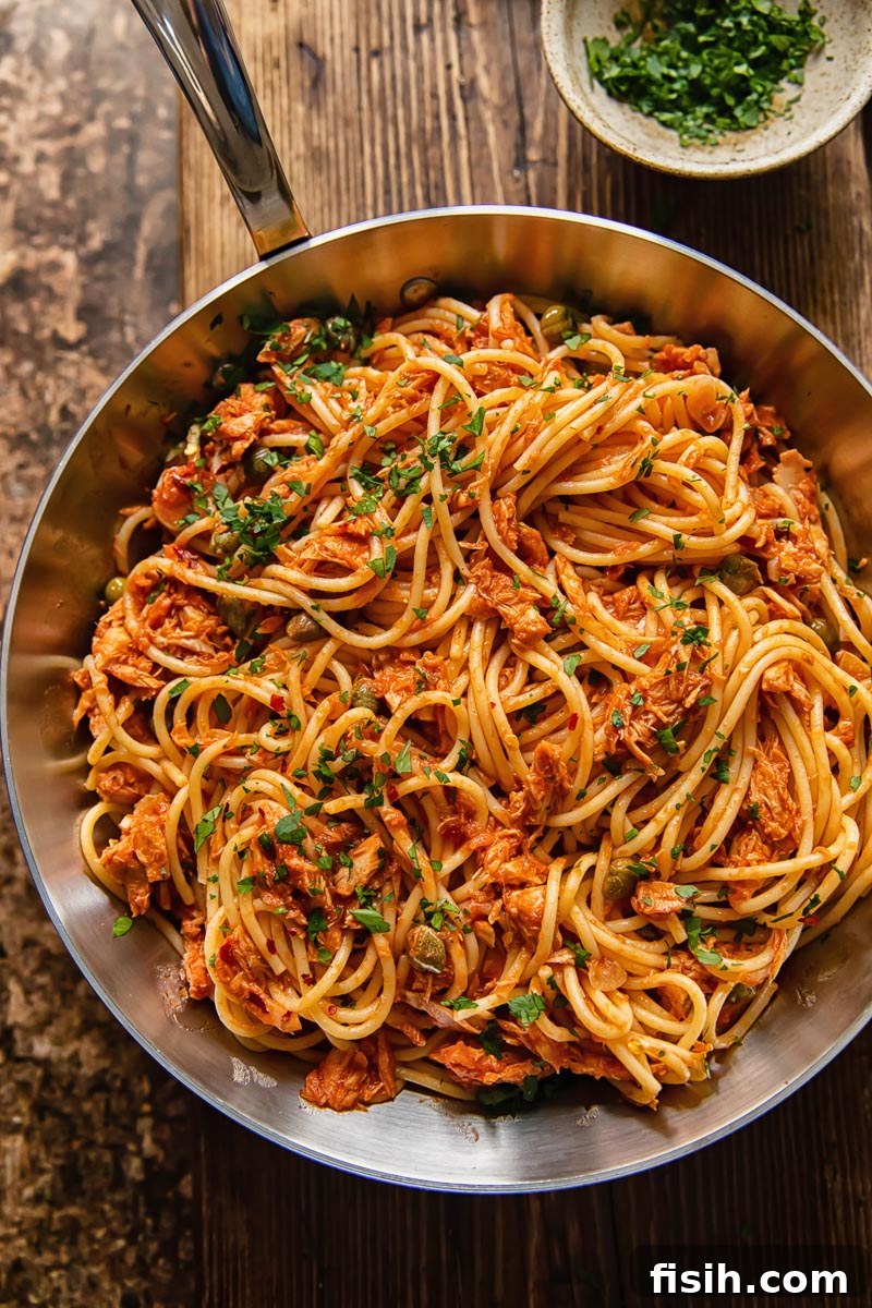 Tangy Tuna Pasta in Minutes 3 Close-up, top-down view of a pan filled with tuna pasta in a vibrant tomato sauce, set on a dark wooden background.