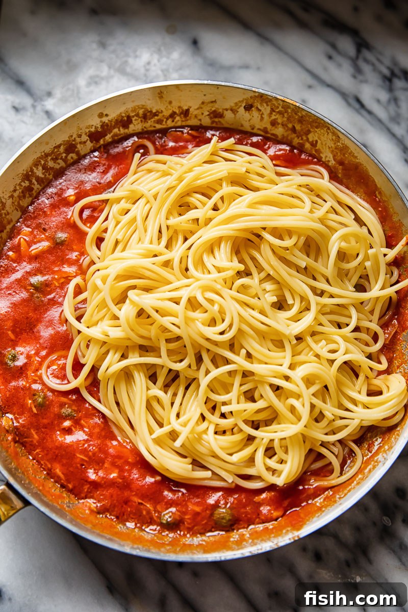 Tangy Tuna Pasta in Minutes 4 Close-up of spaghetti draped over rich red tuna sauce in a cooking pan, ready to be tossed.