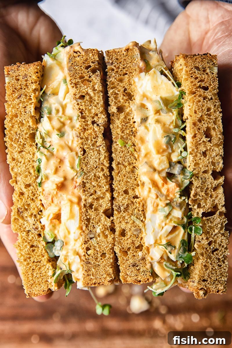 Perfectly cut in half egg salad sandwich revealing creamy filling and fresh greens