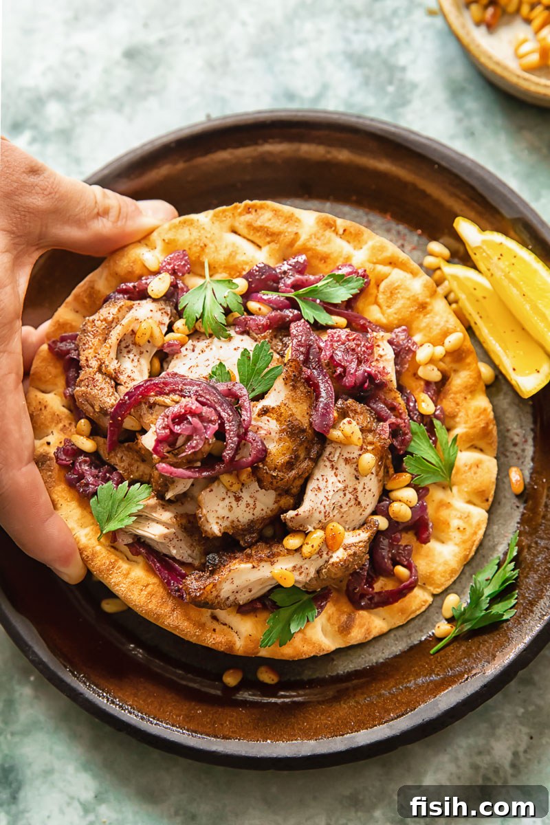 Person grabbing a piece of Chicken Musakhan on flatbread, highlighting the informal, hands-on eating style.