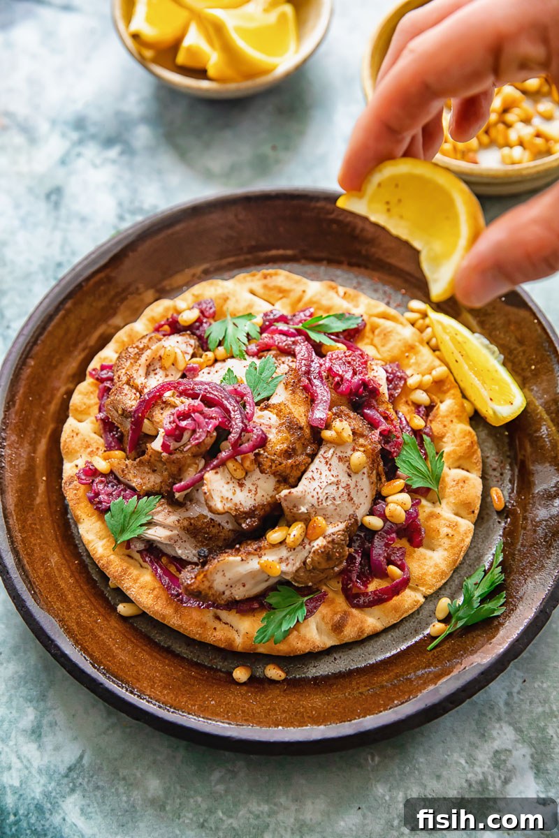 Person squeezing fresh lemon over Chicken Musakhan on flatbread, adding a final touch of zest.