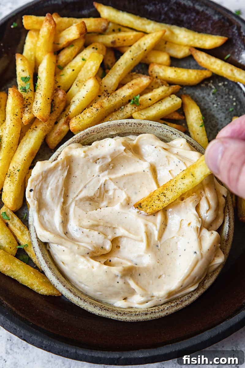 Top down shot of person dipping a fry into truffle aioli dip, highlighting the creamy texture.