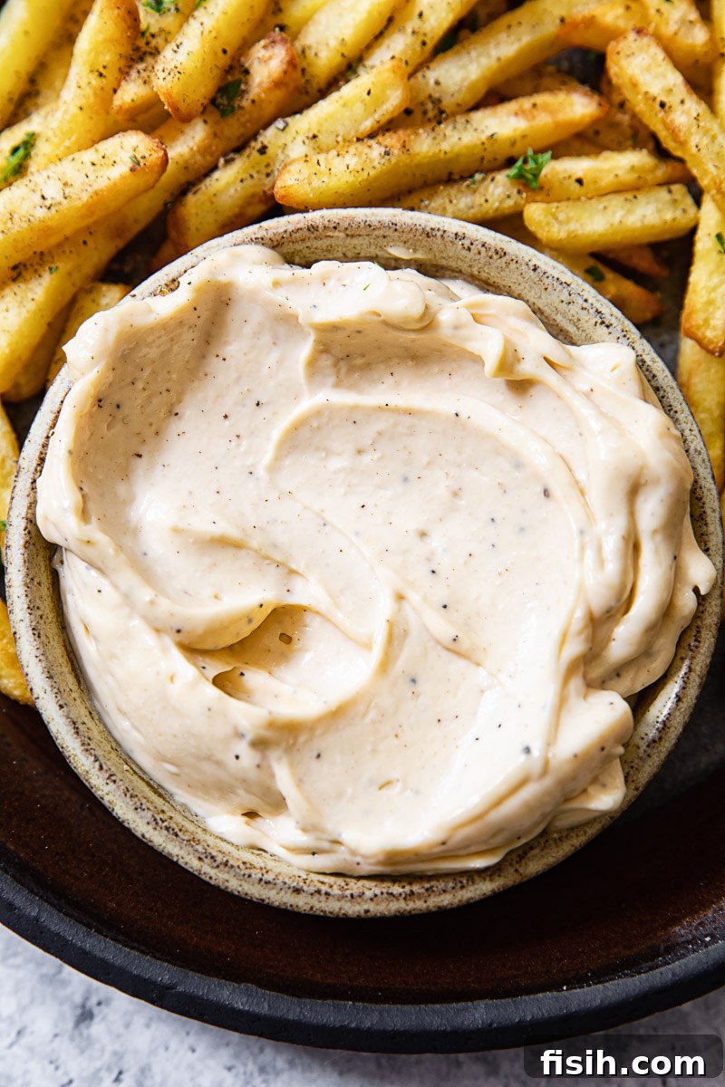 Close up shot of creamy truffle aioli in a white bowl, with golden fries arranged around it.