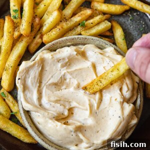 Top down shot of person dipping a fry into truffle aioli dip.