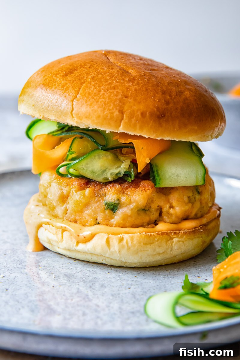 Zesty Salmon Burgers Topped with Spicy Carrot-Cucumber Slaw 5 Side view of a vibrant salmon burger with slaw on a plate
