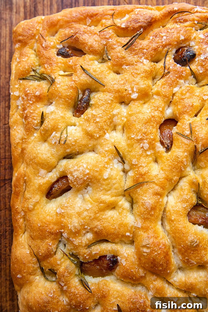 Effortless Artisan Focaccia 2 Top-down view of golden focaccia bread with embedded garlic confit and rosemary, ready to be enjoyed.