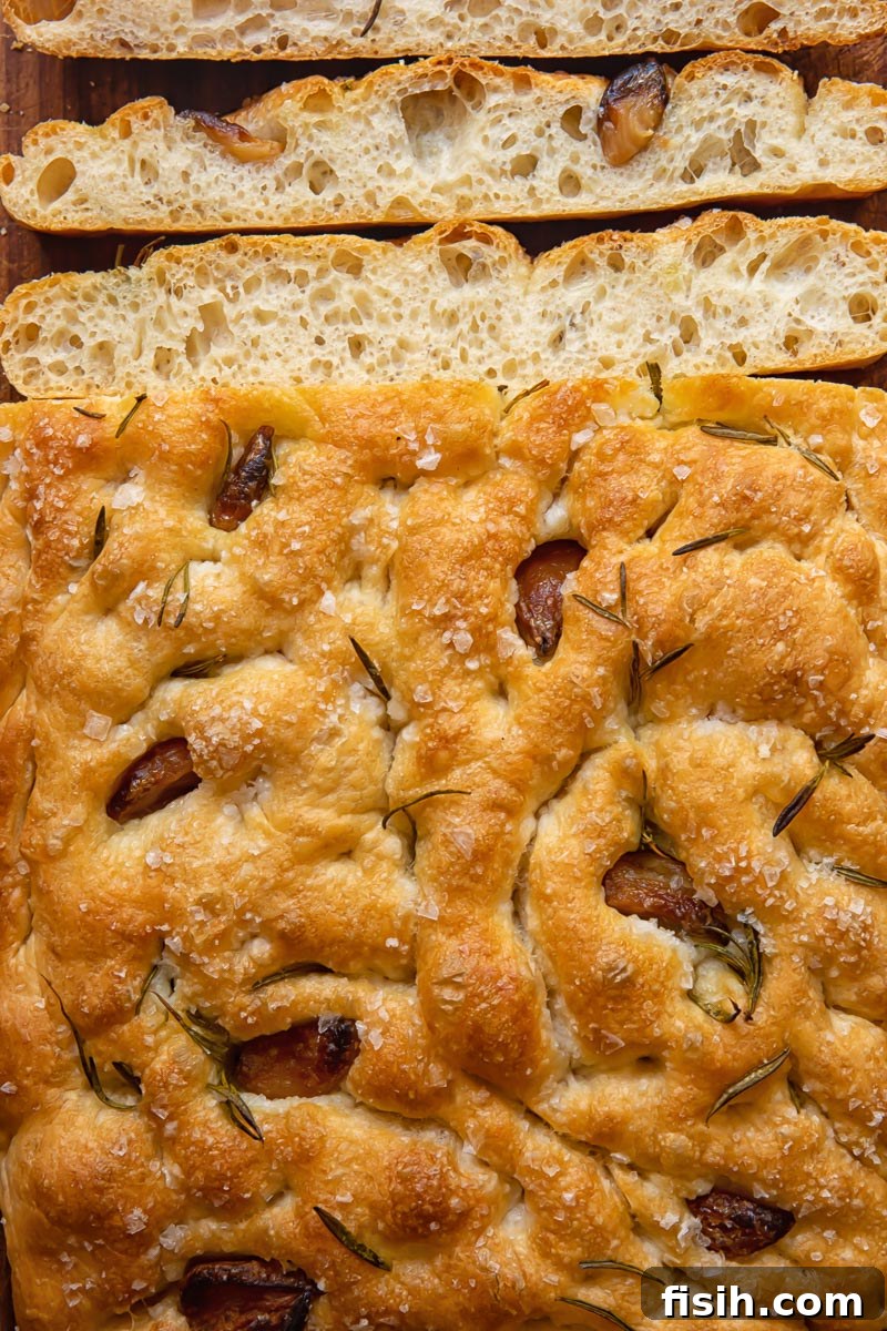 Effortless Artisan Focaccia 3 Freshly baked focaccia bread cooling on a rack, with a few slices already cut, revealing its airy interior.