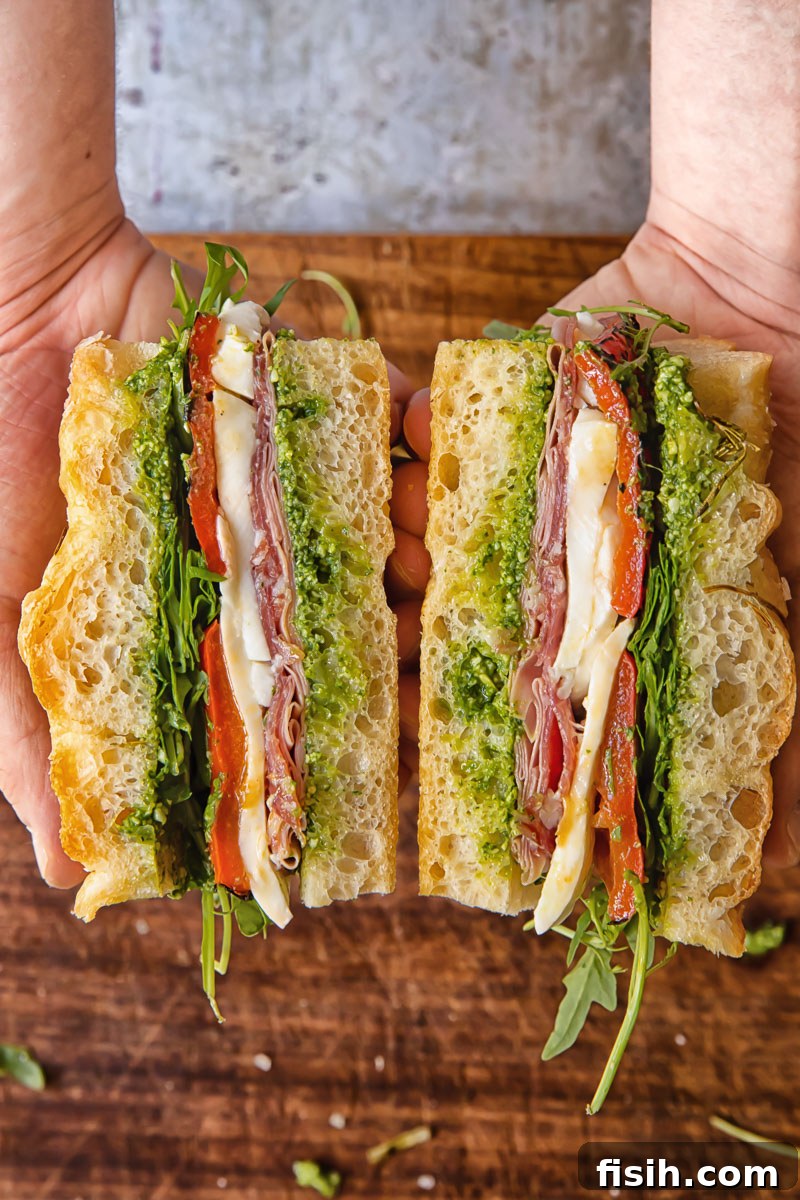 Cross-section of an Italian focaccia sandwich filled with various deli meats, creamy mozzarella, and vibrant pesto, ready to be enjoyed.