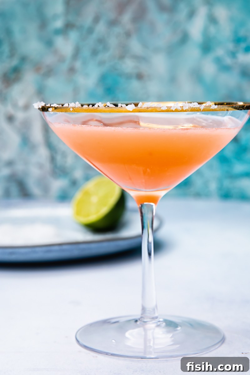Side shot of blood orange margarita in a cocktail glass next to a lime