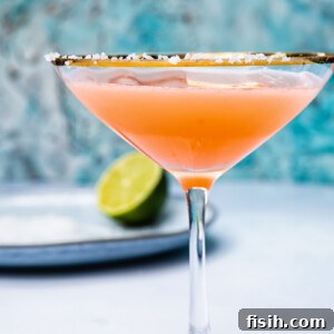 Side shot of blood orange margarita in a cocktail glass next to a lime