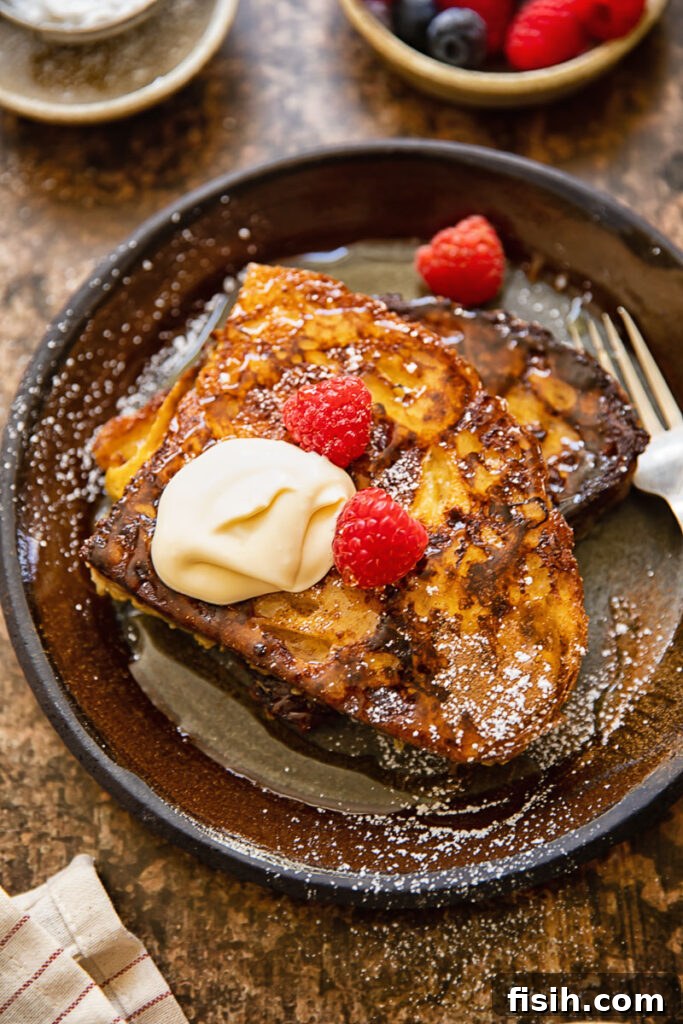 Top down shot of cinnamon sourdough French toast with maple crème fraîche and fresh raspberries on a white plate, ready to be enjoyed for brunch.