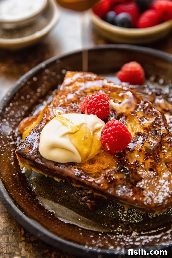 Close up shot of golden maple syrup being generously drizzled over a stack of cinnamon sourdough French toast adorned with maple crème fraîche.