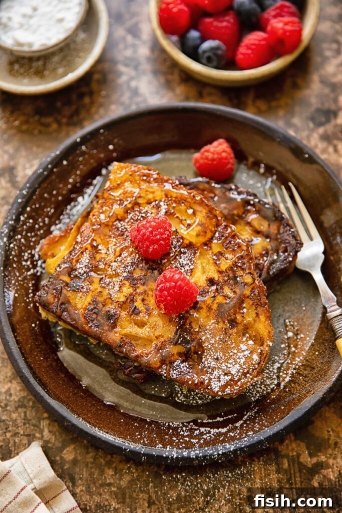 Top down view of a plate of cinnamon sourdough French toast, generously topped with vibrant fresh raspberries and a dusting of powdered sugar.