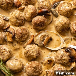 Top down view of spoon scooping meatballs in Marsala sauce from a pan