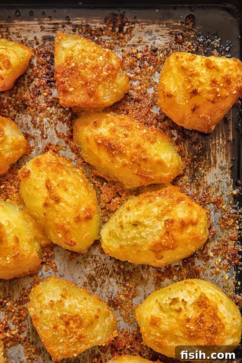Top down view of Parmesan crusted potatoes evenly coated with seasoning on a baking tray, ready for roasting and forming a crispy crust.