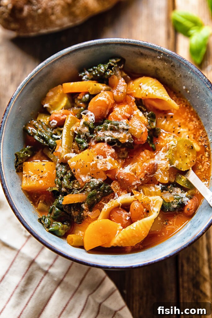 Bowl of minestrone soup with a spoon, garnished with fresh herbs and a drizzle of olive oil, on a rustic wooden table.