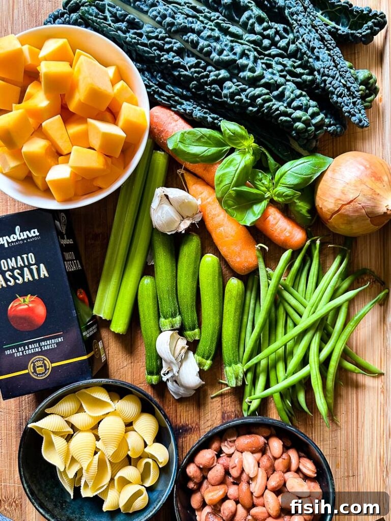 Top down shot of various fresh ingredients on a wooden board, including carrots, celery, onion, kale, squash, beans, and herbs, ready for minestrone soup.