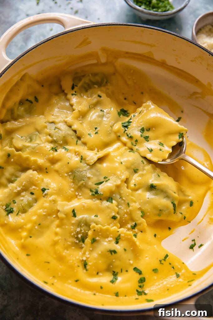 A spoonful of ravioli in a rich butternut squash sauce within a pot of pasta.