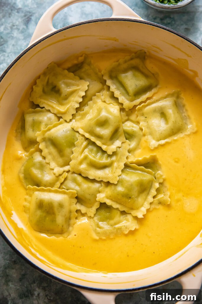 Ravioli parcels resting on a bed of smooth butternut squash sauce in a cooking pot.