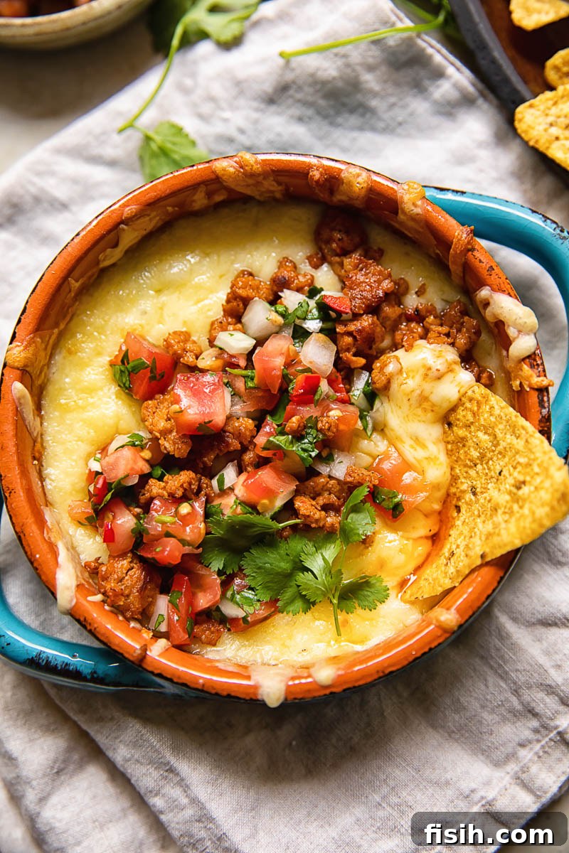 A dish of Queso Fundido with Chorizo, with a single tortilla chip poised to scoop up the melted cheese.