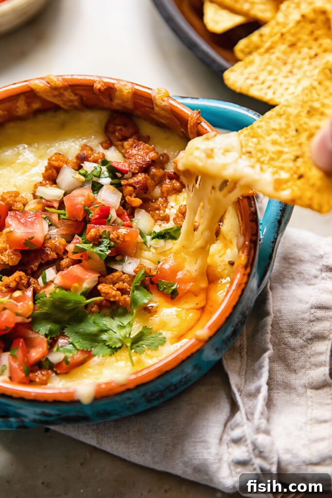 A tortilla chip scooping a generous portion of cheesy, melted Queso Fundido with chorizo.