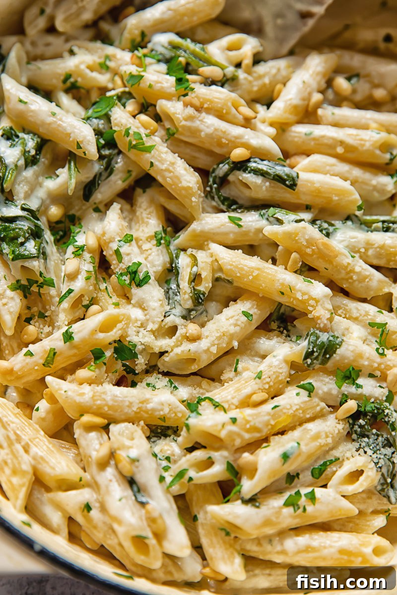 Close-up view of creamy goat cheese pasta mixed with fresh spinach, glistening in a pan, ready to be served.