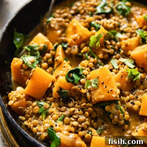 A vibrant, creamy coconut lentil curry with butternut squash in a cooking pan.