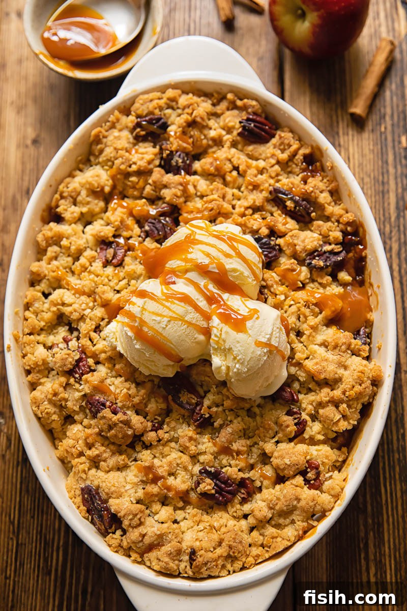 Effortless Apple Crisp from Scratch 2 Top down view of a scoop of vanilla ice cream melting on a warm apple crisp, garnished with toasted pecans, in a ceramic baking dish.