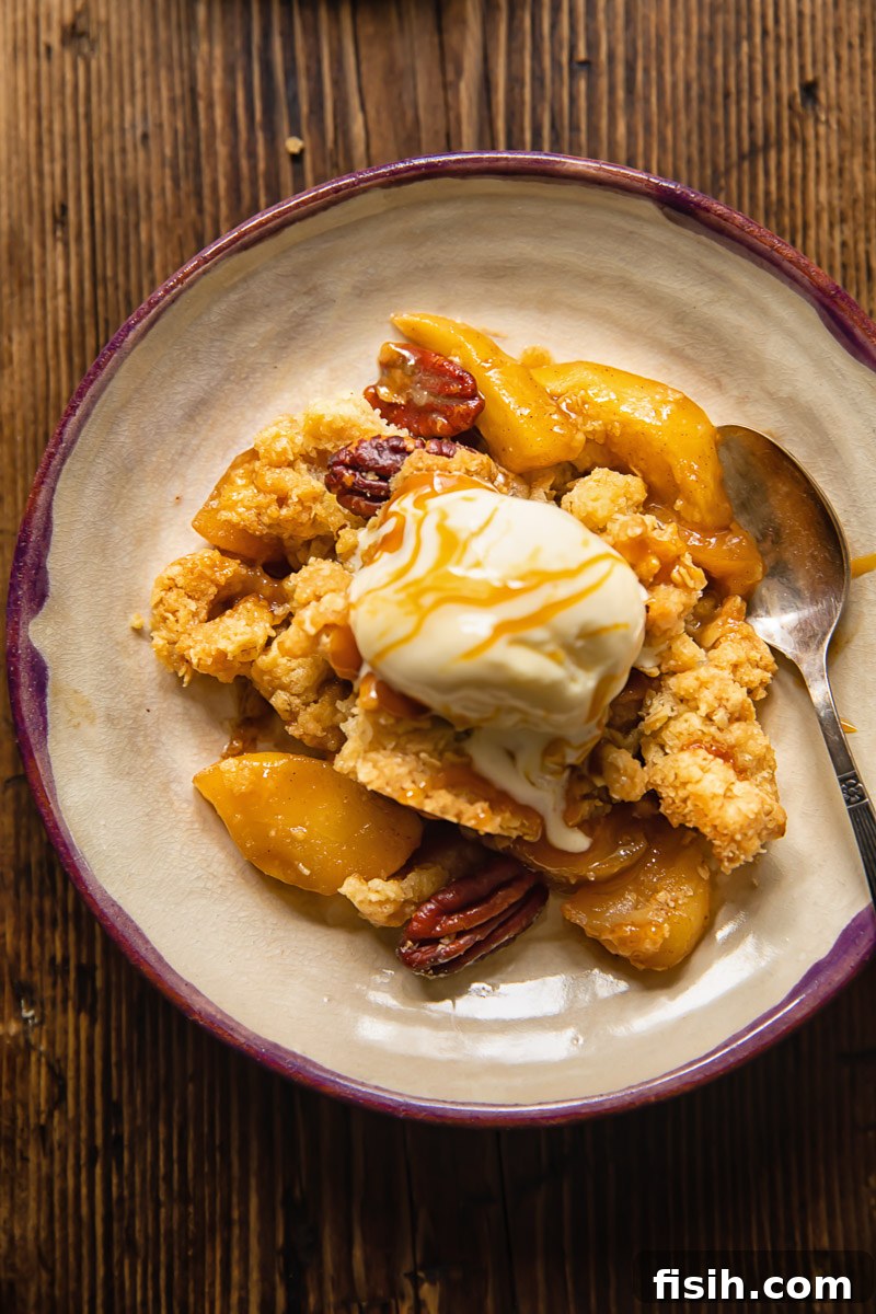 Effortless Apple Crisp from Scratch 3 Close-up shot of a single serving of apple crisp on a white plate, topped with a melting scoop of ice cream and a sprinkle of chopped pecans.