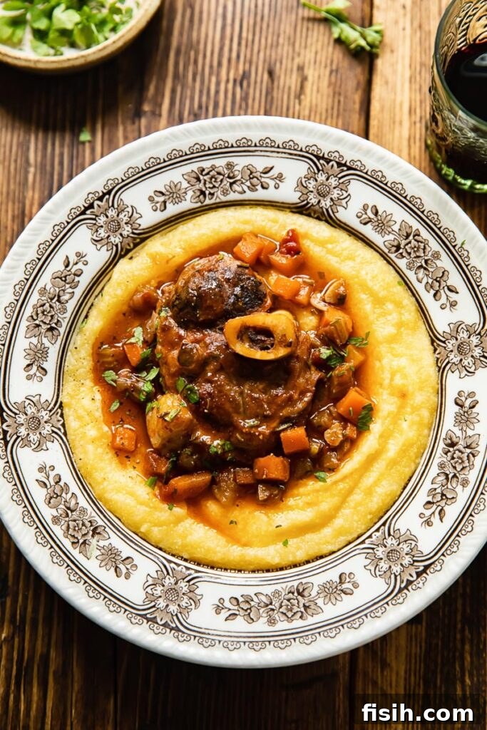 Top down view of pork osso buco served over creamy polenta in a bowl, garnished with fresh herbs.