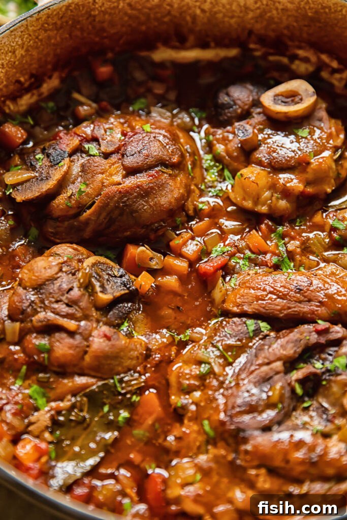 Close up shot of Pork osso buco in a pot with cut up carrots and celery, highlighting the rich braising liquid.