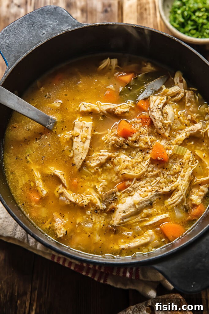 Top down shot of chicken and mushroom soup in a large cooking pot with visible carrots and bulgur, ready to be served.