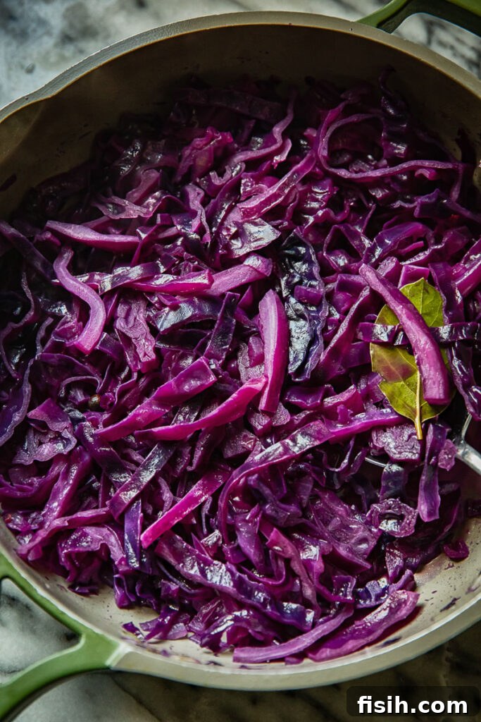 Slow-Simmered Ruby Cabbage 3 Close up view of braised red cabbage being cooked in a large pan, steaming with aromatic spices and bacon