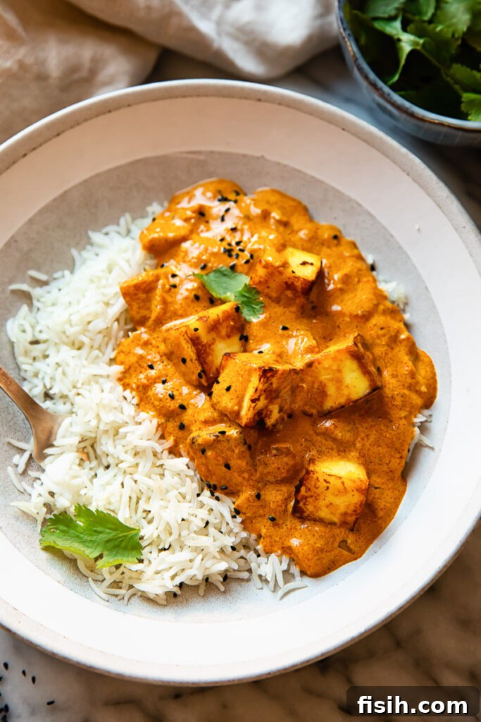 Serving bowl of paneer tikka masala alongside fluffy white basmati rice