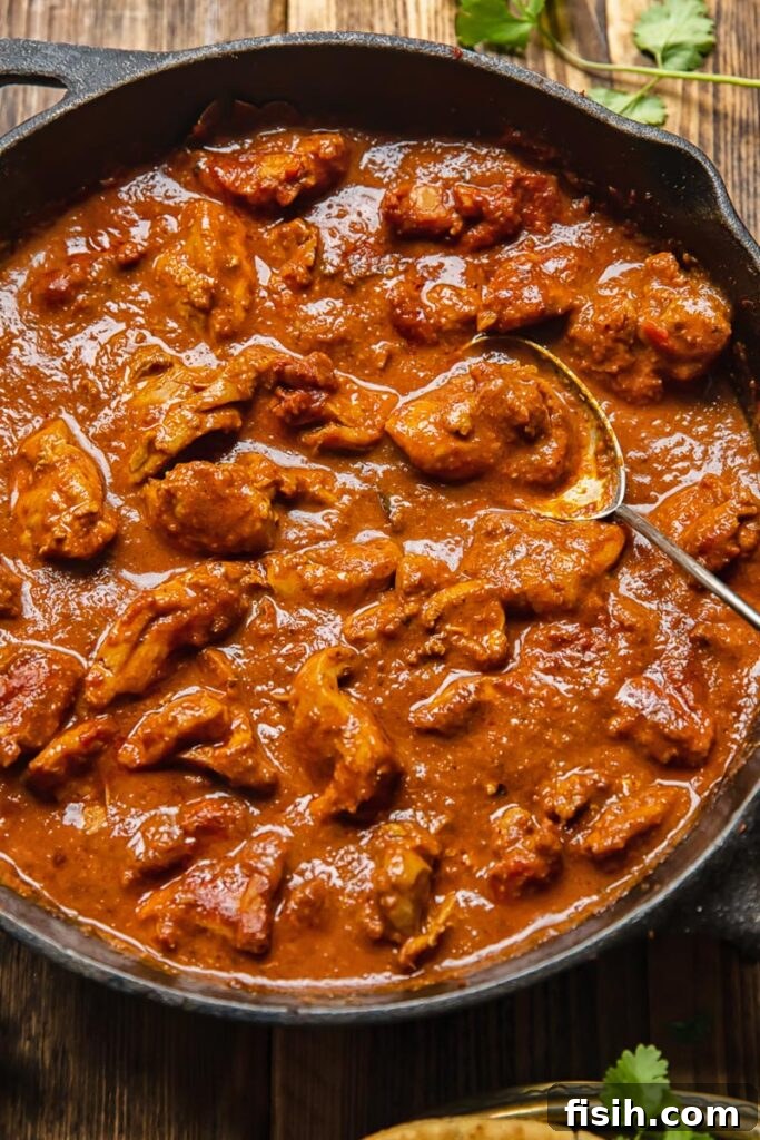 Scarlet Kashmiri Chicken 2 Close-up of a pan of ruby-red Chicken Rogan Josh, ready to be served, with a serving spoon resting inside.