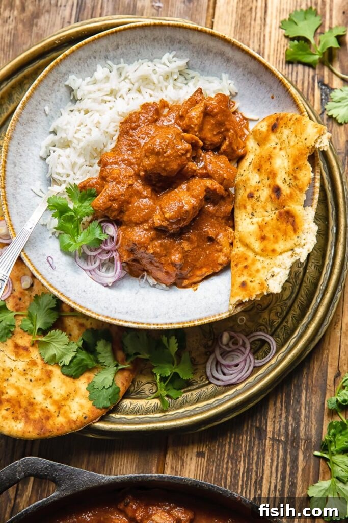 Scarlet Kashmiri Chicken 3 Top-down view of a bowl of chicken rogan josh served over white rice, accompanied by a piece of naan bread.