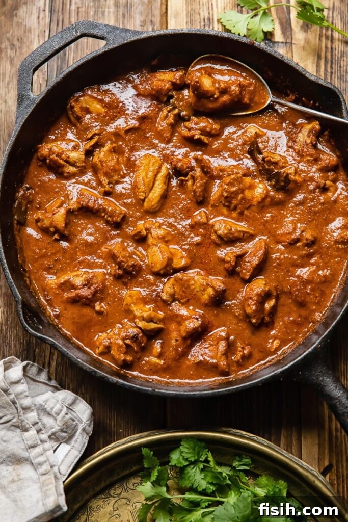 Scarlet Kashmiri Chicken 5 Top-down shot of a large pan of chicken rogan josh resting on a rustic wooden table.