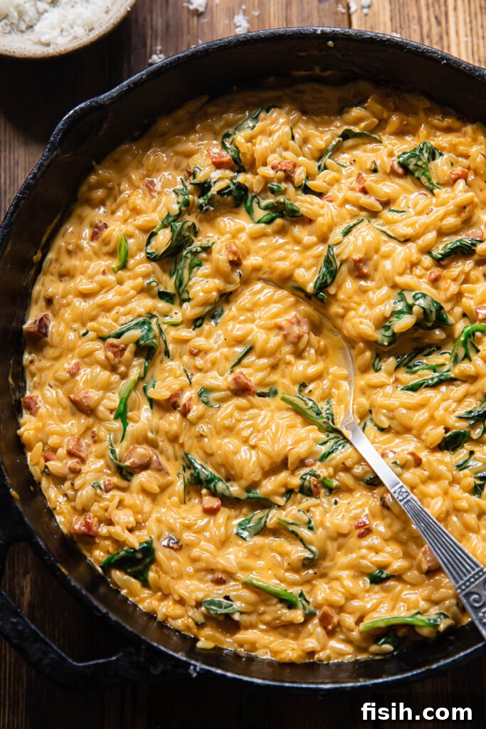 Top down shot of a spoon scooping creamy orzo with chorizo and spinach directly from the cooking pan, showing the steam and inviting texture