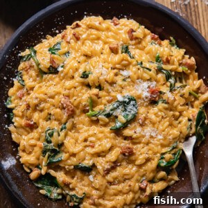 Top down view of creamy orzo with chorizo and spinach on a plate with a fork