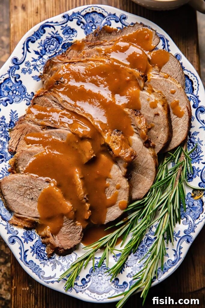 Perfectly Tender Slow Cooker Roast 2 Top down shot of slow cooker roast beef on a plate with gravy and rosemary, highlighting its tenderness and rich color.
