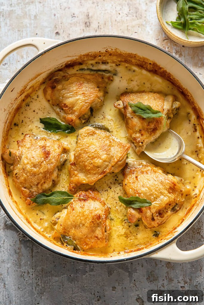 Top down view of spoon scopping creamy sage sauce with chicken thighs in a pot