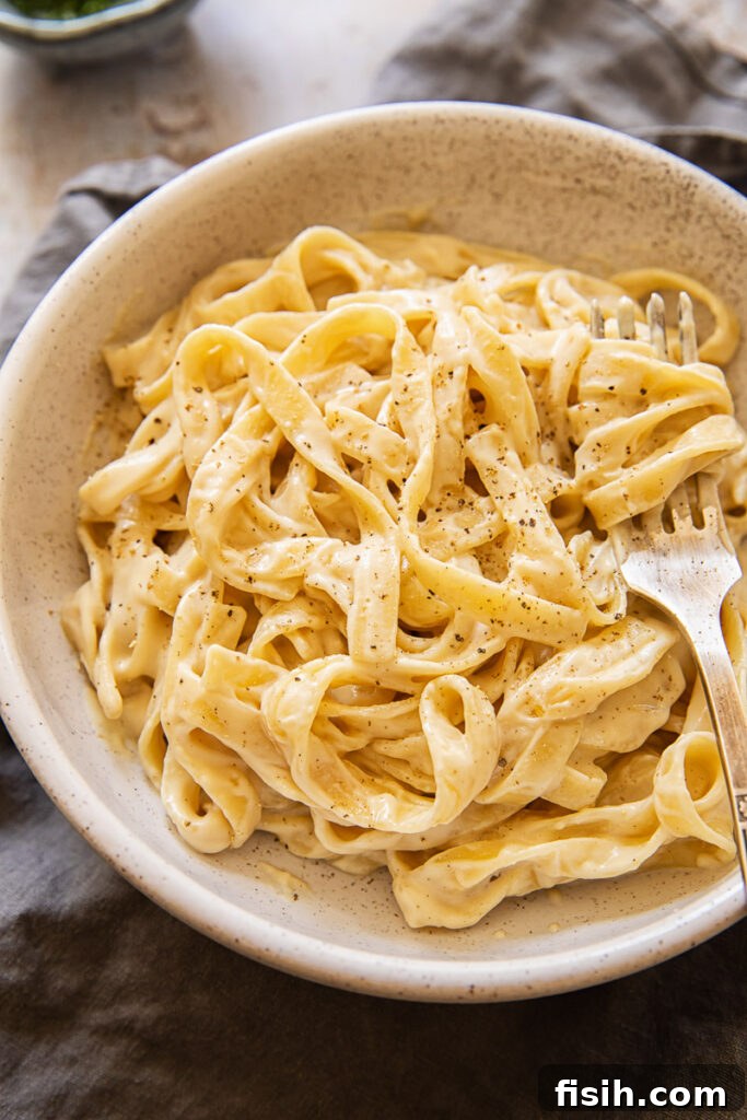 Creamy Vegan Alfredo Sauce 2 Bowl of vegan Alfredo sauce with sprinkling of pepper and a fork