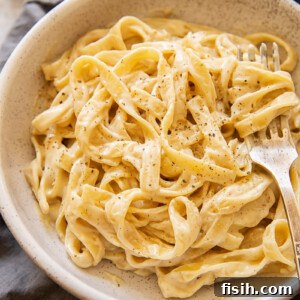 Bowl of vegan Alfredo sauce with sprinkling of pepper and a fork