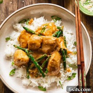 Top down shot of peanut butter chicken on top rice with beans and green onions in a bowl with chop sticks