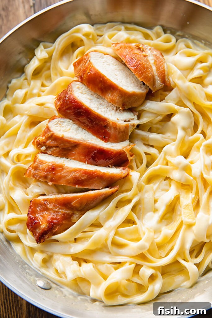 Top down shot of sliced prosciutto wrapped chicken on top of fettucine in alfredo sauce in a bowl