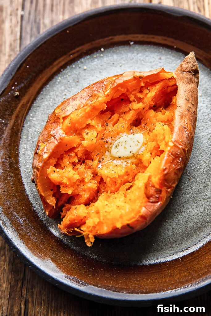 Close up shot of a cut open baked sweet potato topped with melted butter on a plate, showcasing its soft, fluffy interior